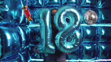 Bir kız 18. yaş gününü parlak mavi balonlar, parlak bir disko arka planı ve neşeli bir parti havasıyla kutluyor..