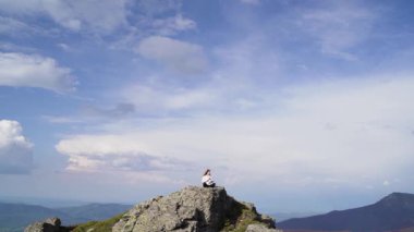 Genç, barışçıl bir kadın dağın tepesinde Zen yoga pozu vererek meditasyon yapıyor. Etrafı çarpıcı bulutlarla çevrili. Bu yüksek irtifa konumunun sakin doğası...