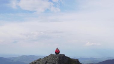 Genç bir kadın Zen yogası pozuyla huzur içinde meditasyon yapıyor. Bir dağın tepesinde, güzel bulutlar gökyüzünde sürükleniyor. Doğadaki bu sakin farkındalık anı odaklanmak için mükemmel bir fırsat.