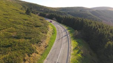 Hava aracının görüntüleri, Bulgaristan 'ın orta kesimindeki Beklemeto Geçidi' nin dolambaçlı dağ yolunda seyreden canlı kırmızı bir arabayı çekiyor. Etrafı yemyeşil tepeler, çam ağaçları ve açık çayırlarla çevrili.