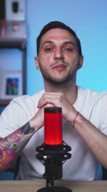 Dövmeli Avrupalı erkek vlogger bir stüdyoda konuşma tarzı bir video kaydediyor. Bağlı ifade ve hikaye anlatma tonu.