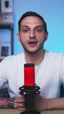 Dövmeli Avrupalı adam, sıcak ışık ve profesyonel ses teçhizatıyla minimal bir podcast stüdyosunda kameraya otantik bir mesaj gönderdi.