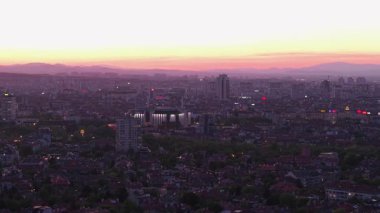 Alacakaranlıkta Sofya Bulgaristan üzerindeki insansız hava aracı, alacakaranlığın yumuşak ışığı altında yeşil bir park ve etrafındaki binaları gösteriyor