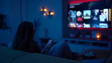 Rahat genç bir kadın gece evde film seyrediyor, patlamış mısır yiyor ve rahat bir film gecesinin tadını çıkarıyor..