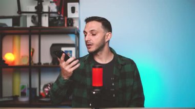 Genç adam akıllı telefonu yüzüne dayayıp yapay zeka destekli bir ses asistanıyla iletişim kuruyor. Modern teknoloji, ses tanıma ve akıllı iletişim kavramı.