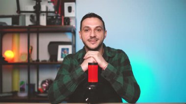 Genç adam rahat ve modern bir stüdyoda yayın yapan bir mikrofona açıkça konuşan ve doğrudan kameraya bağlanan bir podcast bölümü kaydediyor..
