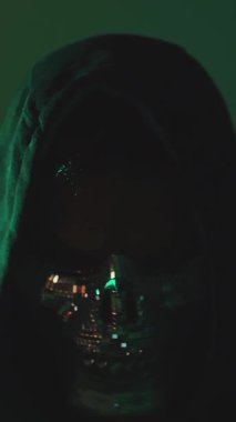 Kapüşonlu maskeli kişinin doğrudan kameraya bakıp karanlık odada çekildiği siber güvenlik tehdidi kavramı.