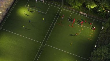 Yukarıdan aşağıya, yeşil ağaçlarla çevrili bir şehir parkında futbol maçını gösteren bir drone fotoğrafı. Sahnede oyuncuların ve aşağıda canlı yeşilliklerin olduğu sinematik kentsel doğa sahnesi.