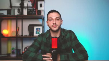 Erkek vlogger ya da podcaster seyircilerine seslenirken, asgari bir stüdyoda profesyonel ses donanımı ile kayıt yaparak sosyal ya da yayın platformları için içerik oluşturur..