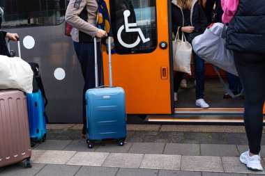 Tramvaylı yolcular bir tren vagonunun açık kapısından girip çıkıyorlar. Kapıdaki engelliler için imzalayın..