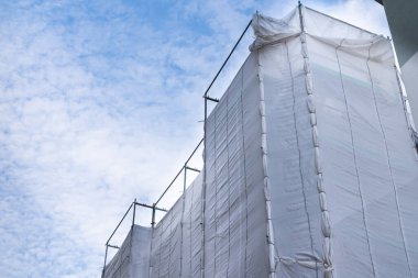 İnşaat alanı beyaz plastik filmlerle kaplı. Açık beyaz bulutlu mavi gökyüzü.