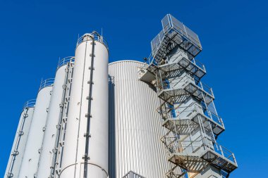 Gökyüzüne uzanan bir endüstriyel binanın silindirik kulesi. Kenarlarında parmaklıklar olan metal merdivenler..