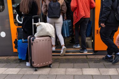 Vagonları ve çantaları olan birçok yolcu bir tren vagonunun açık kapısından içeri giriyor. Alt görünüm.