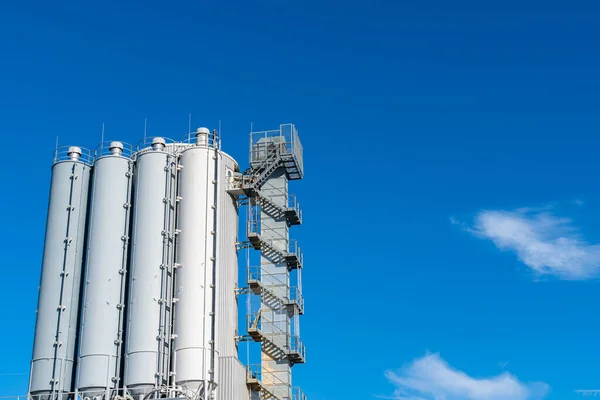 青い空に対する工業ビルの円筒形の塔 横に手すりのある金属製の階段 — ストック写真