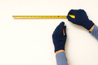 Builders hands with measuring tape and pencil on white wall. Close up.