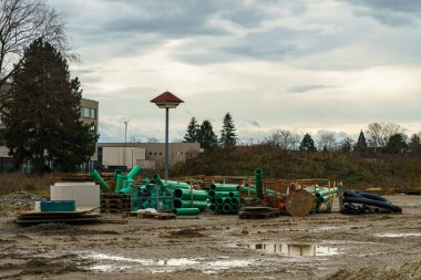 Dirty construction site after rain with a bunch of plastic green pipes. Gray cloudy sky.