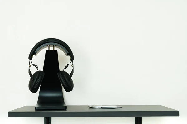 Black headphones on stylish black stands stand on a shelf against a white wall. Copy space.