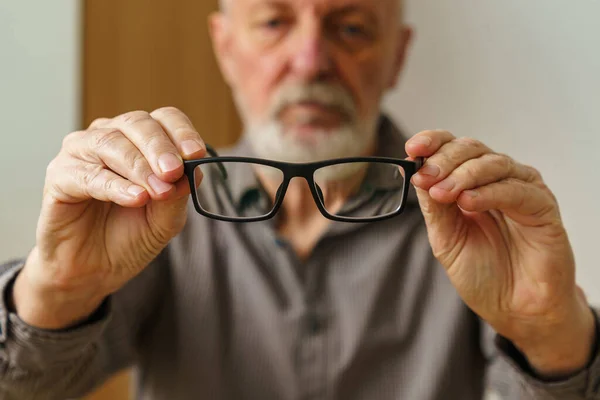 Close up of male hands holding a pair of glasses. Mans face out of focus.
