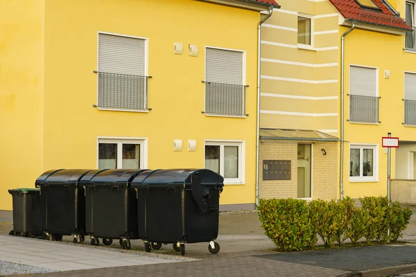 Black trash cans standing near a yellow residential building.