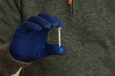 Man hand in blue protective gloves holding a large metal bolt. Close-up.