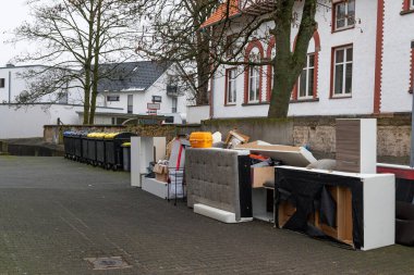 Old damaged furniture on street outside house for transportation to a landfill. Garbage containers in the background.
