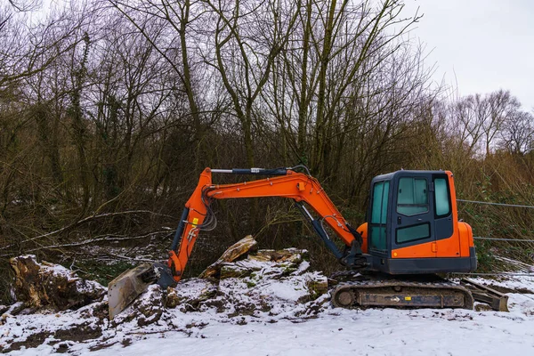 Small excavator raking the ground on a snow-covered construction site.