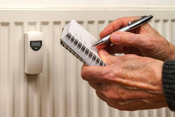 Man's hands recording heat consumption readings on a heating radiator. Close up.