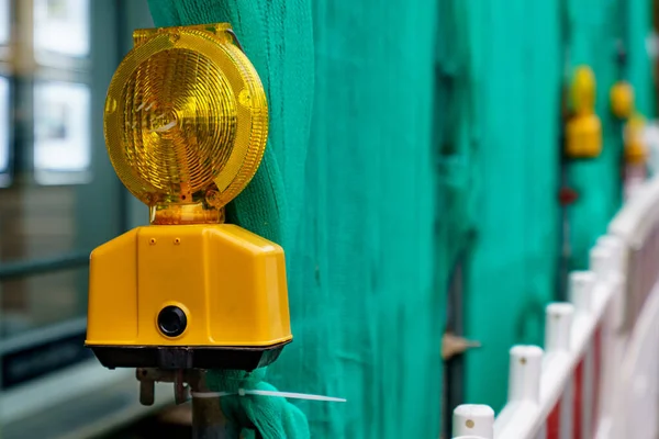 Yellow signal lamp against the background of a green fence of a construction site. Closeup.