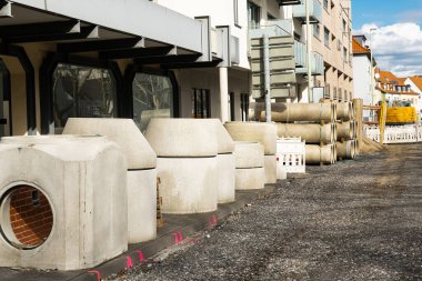 İnşaat alanındaki kaldırımda beton bina yapıları ve boru depoları var..