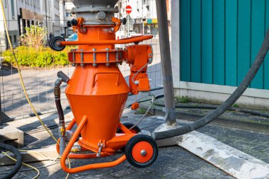 Şehirdeki bir şantiyede motor ve ikmal hortumlarıyla turuncu havan topu karıştırıcısı. Kapat..