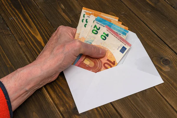 Bir adamın eli, Avrupa para banknotlarını masanın üzerinde duran beyaz bir zarfa koyar. Kapat..
