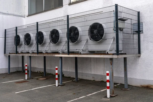 A group of exhaust fans on the wall of a building fenced with a metal grate.