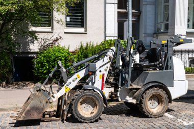 Küçük beyaz bir kazıcı, apartman girişinin yanındaki kaldırımda duruyor..