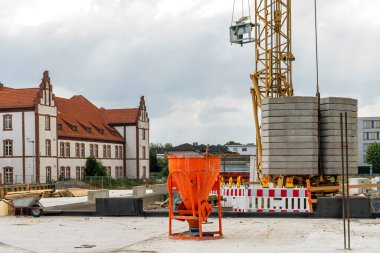İnşaat vinci ve turuncu çimento harç karıştırıcısı olan bir inşaat alanı. Arka planda bulutlu gökyüzünün altında inşa ediliyor.