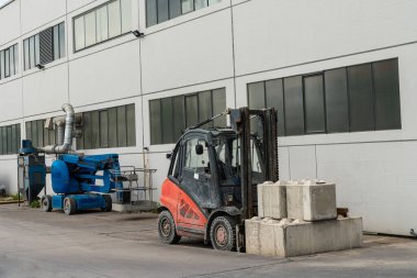 Binanın yanında beton bloklu küçük bir forklift duruyor. İnsanlar için asansörün yanında..