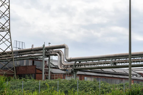 Industrial area with air-stretched metal pipes and building. The sky is covered with clouds.