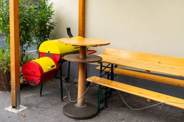 Masası olan ahşap bir bank ve evin duvarının yanında parlak sarı bir duman ızgarası..