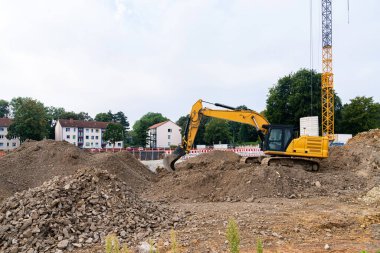 İnşaat alanındaki sarı bir kazıcı büyük toprak yığınlarını kazıyor..