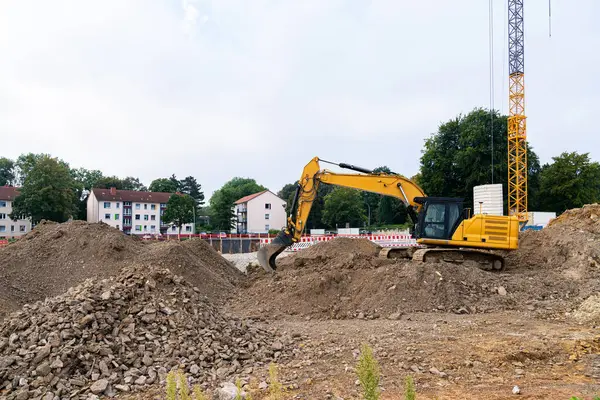 İnşaat alanındaki sarı bir kazıcı büyük toprak yığınlarını kazıyor..