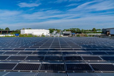 Endüstriyel alandaki birden fazla güneş panelinin görüntüsü. Mavi gökyüzü ve ışık bulutları.