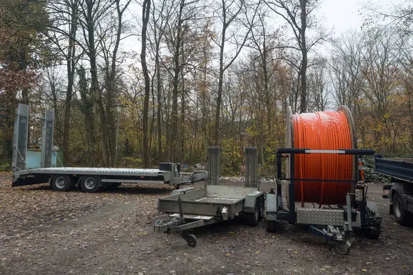 Car trailers and wooden reel with orange cable on autumn forest background.