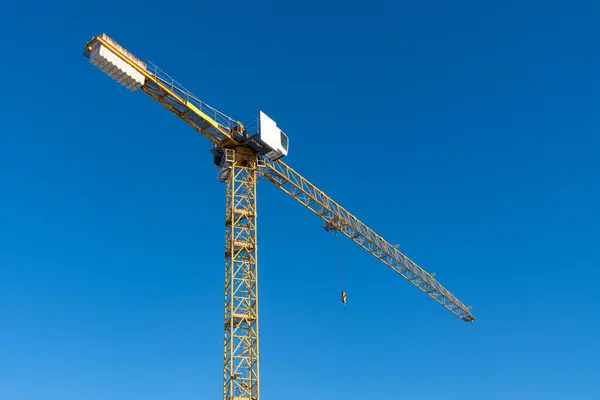 Bottom view of the boom and cabin of a construction crane against a blue sky.