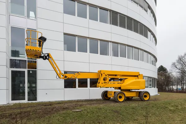 A bright yellow aerial work platform against a white building background.