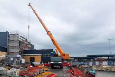 İnşaat halindeki yeni bina iskeleyle çevrili ve inşaat alanında bir kamyon vinci var..