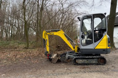 Çıplak sonbahar ağaçlarının arka planında duran küçük sarı bir kazıcı..