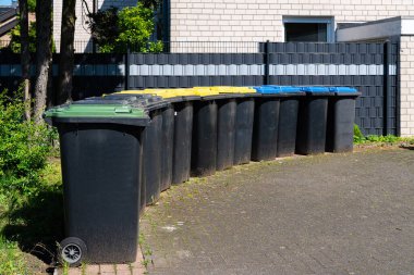 Ayrı atık toplama için plastik kutular bir konut binasının çitleri boyunca dizilmiştir. Çöp kapakları farklı renklerde.