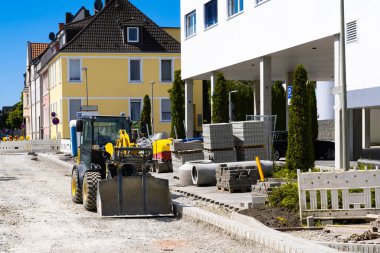Bir yol tamir sahasında paletlerin üzerinde bir kova ve yol levhaları olan küçük bir yükleyici..