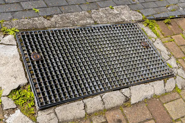 stock image Metal storm drainage grate on a stone-paved sidewalk. Close-up.