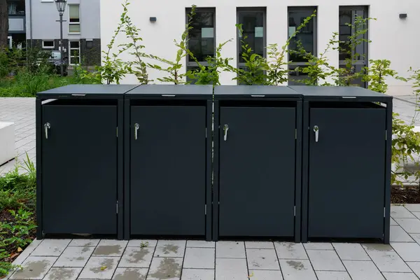 Almanya 'da bir apartmanın beton zemininde duran 4 çöp tenekesi için siyah açık hava kavramsal depolama..