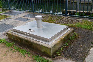 Metal boruları ve bağlantı noktaları olan bir şehir parkının zeminindeki alüminyum su odası bir nehir kıyısının yanına yerleştirilmiş..